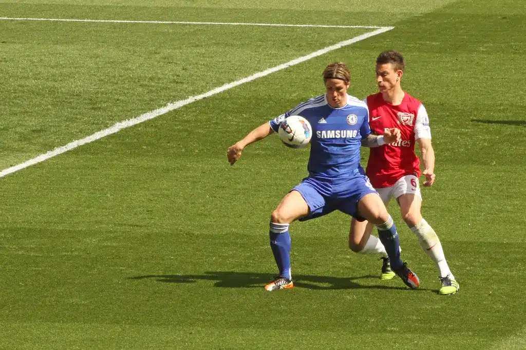 Fernando Torres v modrém dresu Chelsea zpracovává fotbalový míč a za ním stojí Laurent Koscielny.