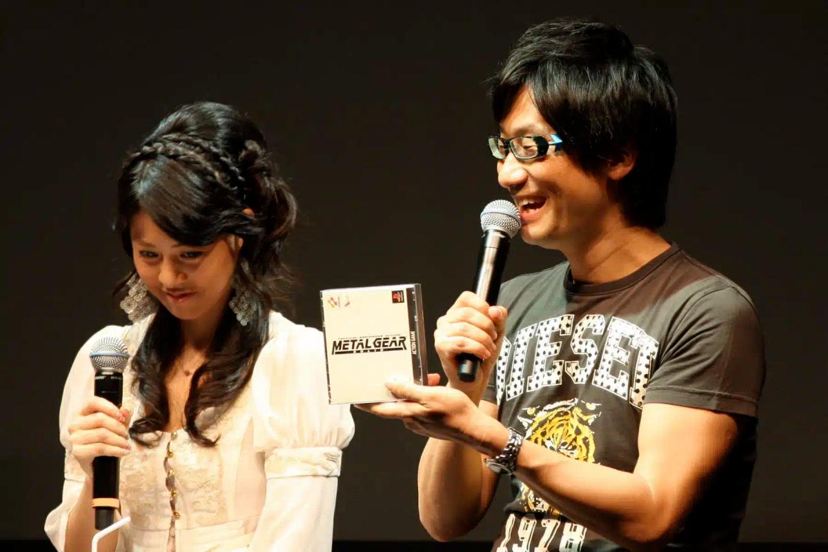 Hideo Kojima drží obal hry Metal Gear a mluví do mikrofonu.
